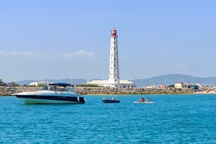 Lighthouse with boats and kayak in blue water under clear sky.