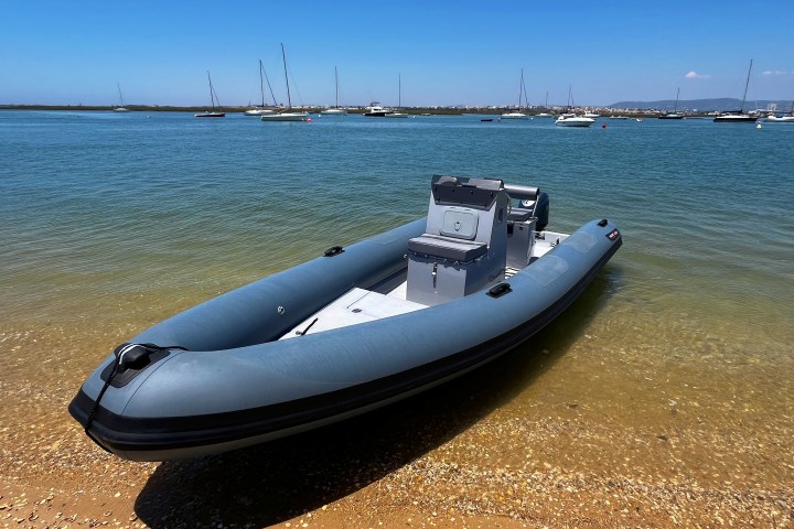 Inflatable motorboat on a sandy shore with sailboats in the background.