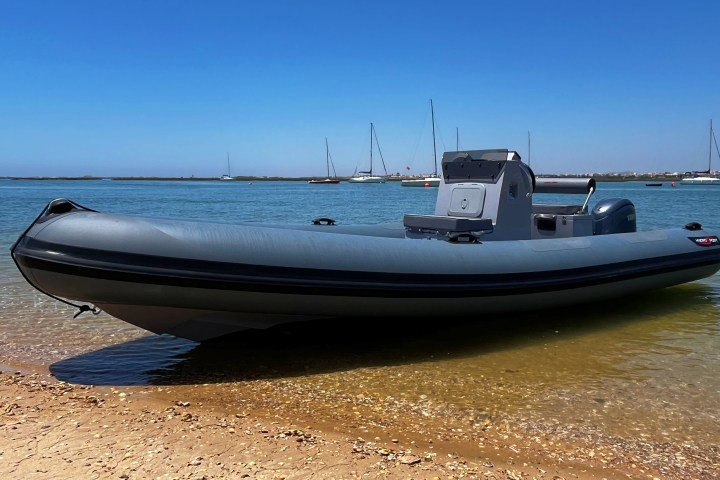 Inflatable boat on sandy shore with sailboats in background.