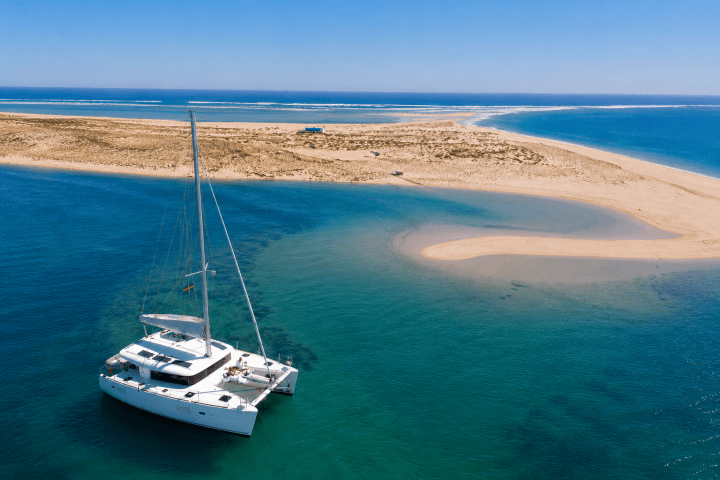 Sailboat in blue water near sandy island with clear sky.