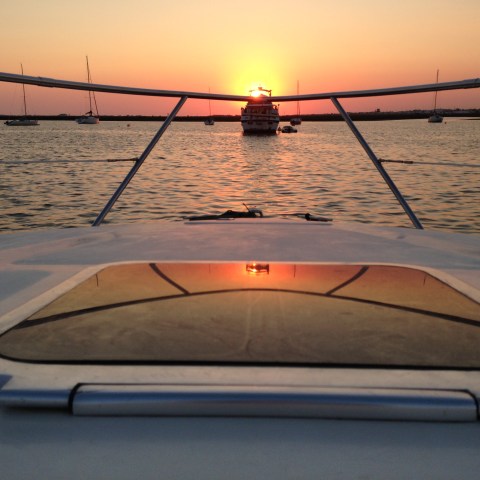 Boat deck view with sunset over calm water and anchored boats.