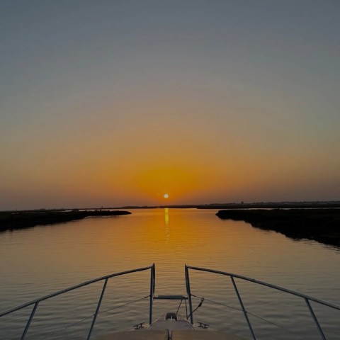 Boat sailing towards sunset on calm water.