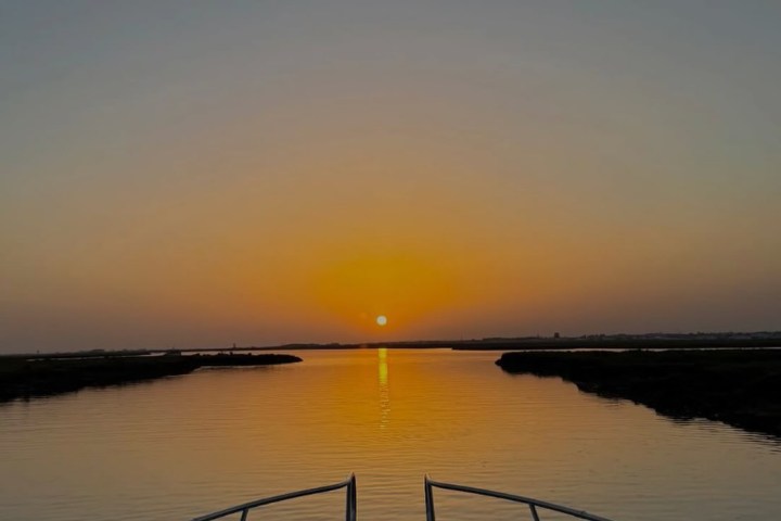 Boat sailing towards sunset on calm water.