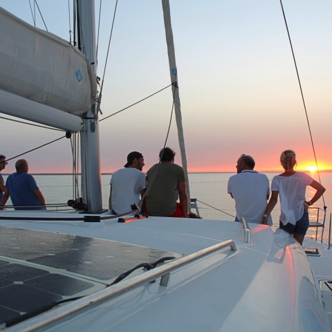 People on a sailboat watching the sunset over the ocean.