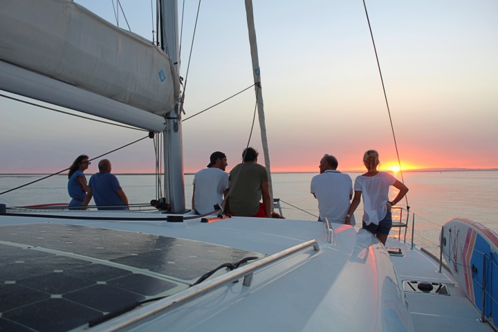 People on a sailboat watching the sunset over the ocean.