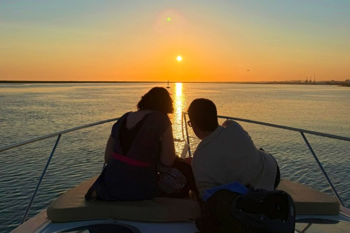 Two people sit on a boat watching sunset over water.