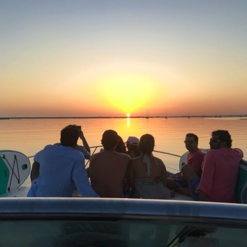 Group on boat at sunset, calm water, clear sky.
