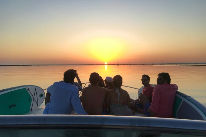 Group on boat at sunset, calm water, clear sky.