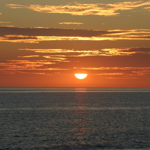 Sunset over the ocean with scattered clouds in the sky.