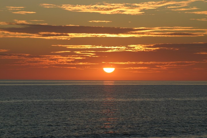 Sunset over the ocean with scattered clouds in the sky.