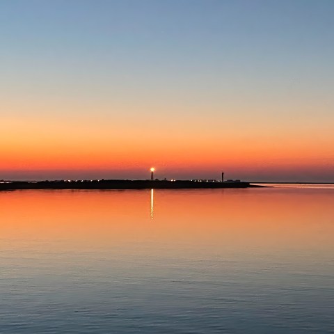 Sunset over calm water with lighthouse and colorful sky.