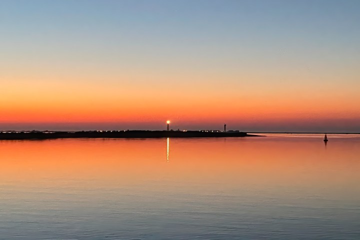 Sunset over calm water with lighthouse and colorful sky.