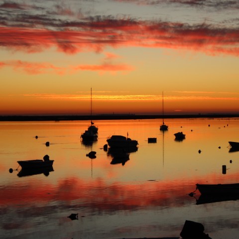 Boats silhouetted on a reflective lake at sunset with red clouds in the sky.