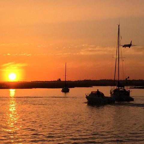 Boats on water at sunset with plane flying overhead.