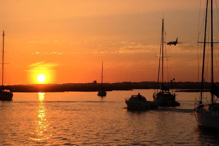 Boats on water at sunset with plane flying overhead.